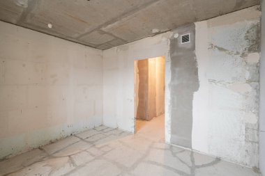 Tasarım için içi boş, gri beton duvar. Boş oda. Mesaj ve resim için boşluk. Beton duvarlar, döşemeler, yeni bir konut binasının içi. Yeni bir dairede bölümler.