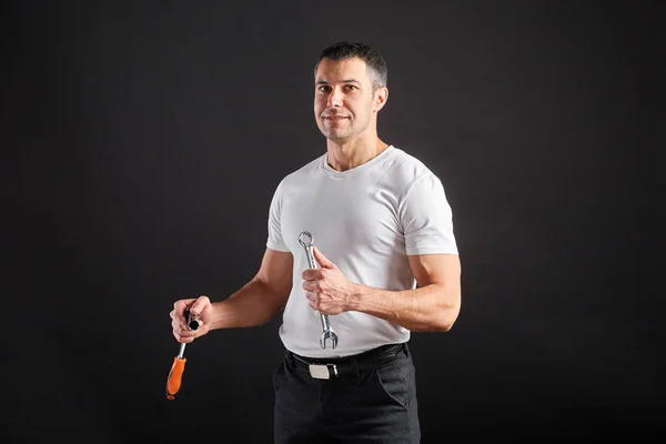 Uomo atletico con chiave inglese su sfondo nero. Non un tipico operaio, con t-shirt e pantaloni bianchi . — Foto Stock