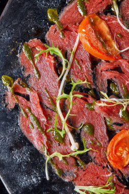 Pesto soslu biftek carpaccio ve siyah masada domates. Restoran menüsü, doğal ve organik gıda konsepti..