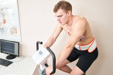 Erkek hasta, kalp fonksiyonlarını kontrol etmek için bisiklet ergometre stres test sistemi üzerinde pedal çeviriyor. Sporcu, doktor tarafından izlenen bir tıbbi çalışmada kardiyak stres testi yapıyor..