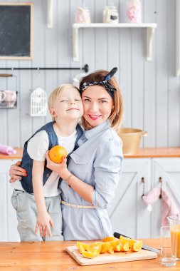 Anne ve oğlu mutfakta kahvaltı ederken gülümsüyorlar. Mutfakta aydınlık bir sabah. Sağlıklı kahvaltı gevrekleri ve taze meyve..