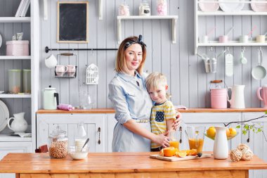Anne ve oğlu mutfakta kahvaltı ederken gülümsüyorlar. Mutfakta aydınlık bir sabah. Sağlıklı kahvaltı gevrekleri ve taze meyve..