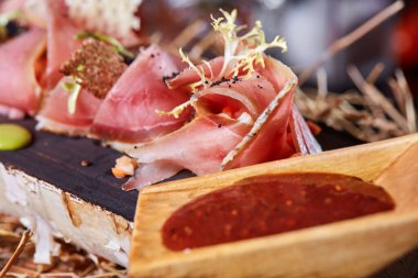Tahta tabakta Antipasto yakın çekim. Domates soslu soğuk füme et tabağı, dilimlenmiş jambon, jambon, pastırma. Ahşap tepside aperatif. Kesilmiş ağaç taklidi..