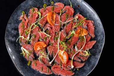 Biftek carpaccio soslu ve domatesli siyah masa. Restoran menüsü, doğal ve organik gıda konsepti..
