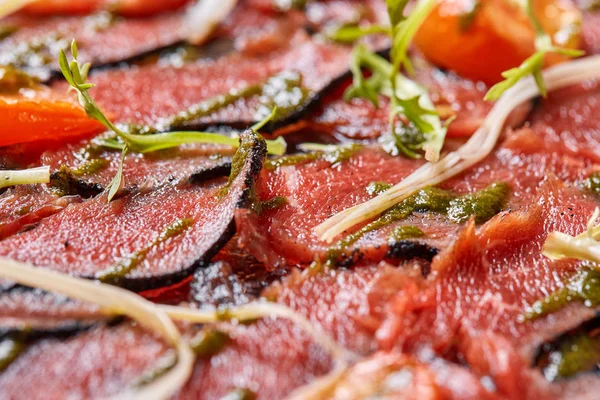 Карпаччо из говядины с песто-соусом и помидорами на черном столе. Меню ресторана, натуральные и органические продукты питания . — стоковое фото