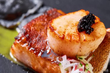 Deniz tarağı ve ravioli. Deniz ürünleri, turna balığı, havyar ve siyah hamur köfteleri yakın plan karanlık bir masada. Sağlıklı yemek..