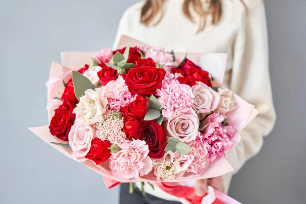 European floral shop. Red and pink Beautiful bouquet of mixed flowers in womans hands. the work of the florist at a flower shop. Delivery fresh cut flower. — Stock Photo, Image