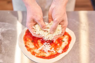 Pizza pişiriyorum. Hamur preformundaki peynir malzemelerini düzenler. Mutfakta üniformalı beyaz önlüklü aşçının yakın çekimi.