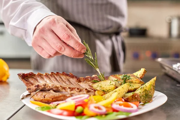 decorated with a sprig of rosemary. the chef prepares in the restaurant. Grilled rack of lamb with fried potatoes and fresh vegetables