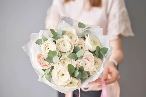 Persian buttercup in womans hands. Bunch pale pink ranunculus flowers with green eucalyptus. The work of the florist at a flower shop