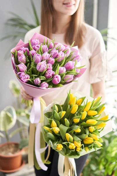 Dos hermosos ramos de tulipanes en manos de mujeres. el trabajo de la floristería en una florería. Entrega flor cortada fresca. Tienda floral europea . — Foto de Stock