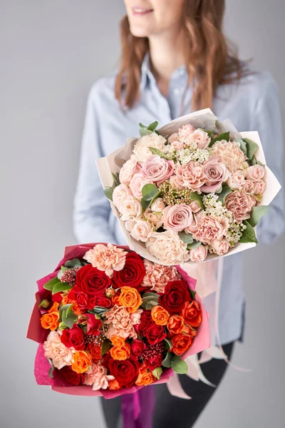 Två vackra buketter av blandade blommor i kvinnors händer. blomsterhandlarens arbete i en blomsteraffär. Leverera färsk snittblomma. Europeisk blomsteraffär. — Stockfoto