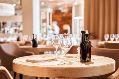 Ön planda şarap bardakları var. Masa ve sandalyeler misafirler için çatal bıçak takımı ve çanak çömlek ile servis edildi.