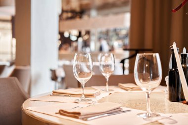 Ön planda şarap bardakları var. Masa ve sandalyeler misafirler için çatal bıçak takımı ve çanak çömlek ile servis edildi.