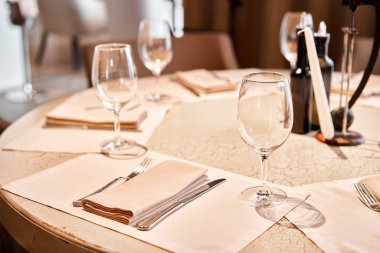 Ön planda şarap bardakları var. Masa ve sandalyeler misafirler için çatal bıçak takımı ve çanak çömlek ile servis edildi.