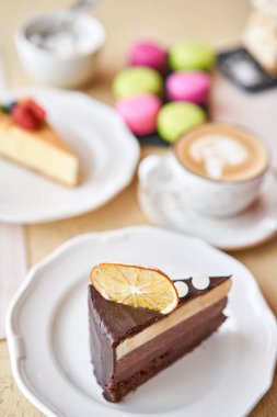 Çikolatalı kek, kremalı, portakal dilimi ve kremayla süslenmiş. Kafede kahvaltı, sabah kahvesi. Tahta masada..