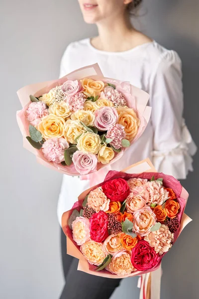 Două buchete frumoase de flori mixte în mâinile femeilor. Lucrarea florarului la un magazin de flori. Livrare flori proaspete tăiate. Magazin floral european . — Fotografie, imagine de stoc