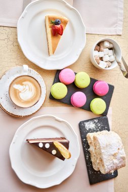 Breakfast in the cafe, morning coffee. Cappuccino and lots of desserts on the table. Napoleon, chocolate cake, cheesecake and macaroons.
