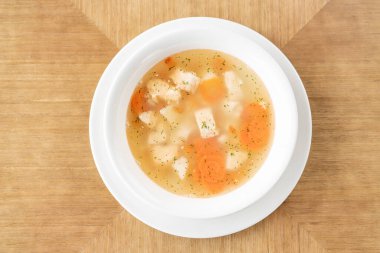 Fish soup in a white plate. Fish soup with vegetables, celery in a cup for the broth. Pike perch and salmon. Plate on wooden table. Restaurant menu