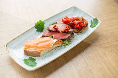 Biftek, domates ve somon. Masada çeşitli abur cuburlar ve antipastalar var. Restoran menüsü. İtalyan mutfağı