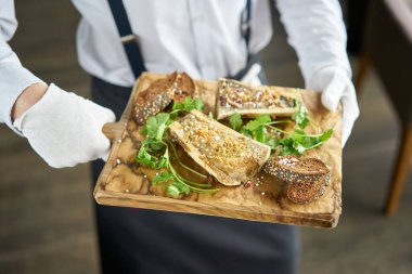 Garson elinde Chimichurri soslu biftek ve kızarmış çörek tabağı tutuyor. Tahta doğrama tahtasında servis edilmiş. Menü Bbq Restoranı