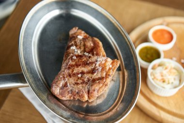 Garson elinde ızgara çizgili biftek, yanında lahana turşusu ve iki sos tutuyor. Striptiz bifteği, aynı zamanda New York bifteği. Tahta bir tahtanın üzerinde hizmet veriyor. Barbekü restoran menüsü.