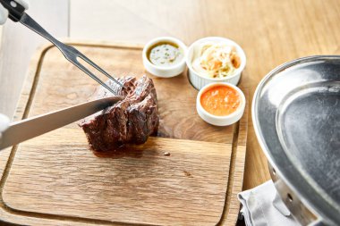 Garson bir bıçakla ızgara et kesiyor. Izgara biftek, lahana turşusu ve iki sos. Tahta bir tahtanın üzerinde hizmet veriyor. Barbekü restoran menüsü.