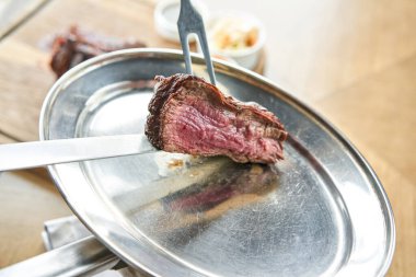 Garson bir bıçakla ızgara et kesiyor. Izgara biftek, lahana turşusu ve iki soslu barbekü restoranı menüsü..