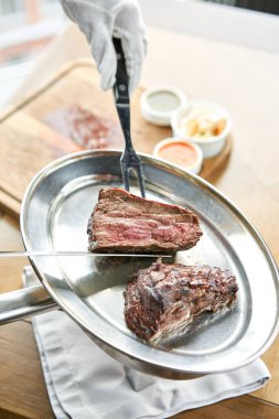Garson bir bıçakla ızgara et kesiyor. Izgara biftek, lahana turşusu ve iki soslu barbekü restoranı menüsü..