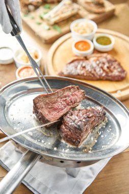 Garson bir bıçakla ızgara et kesiyor. Izgara biftek, lahana turşusu ve iki soslu barbekü restoranı menüsü..