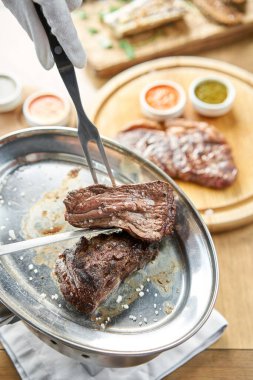 Garson bir bıçakla ızgara et kesiyor. Izgara biftek, lahana turşusu ve iki soslu barbekü restoranı menüsü..