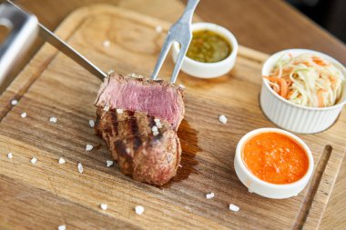 Garson bir bıçakla ızgara et kesiyor. Kızarmış sığır filetosu şatobriyan ve madalyon bifteği turşulu lahana ve iki sosla birlikte. Tahta bir tahtada hizmet etmek..