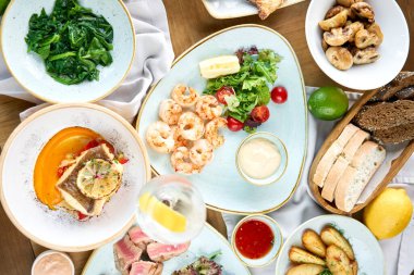 Masada bir sürü farklı lezzetli yemek var. Masada çeşitli abur cuburlar ve antipastalar var. Süslü deniz ürünleri tabağı. Tabakların çeşitleri masada. Restoran menüsü.