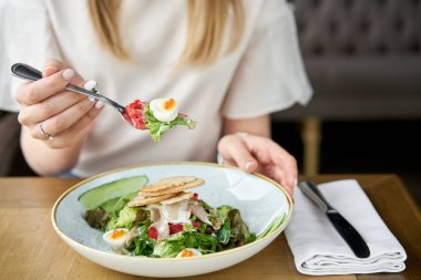 Kadın kuzu dili, salatalık ve bıldırcın yumurtası ile Olivier salatası yiyor. Ahşap masa arka planı. Menü restoranı. Rus geleneksel salatası