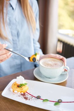 Kadın sarı kremalı pasta yiyor. Fransız tatlısı, yabanmersini, nane şekeri ve beyaz tabakta bir parça krema. Zarif dekore edilmiş. Restoran menüsü