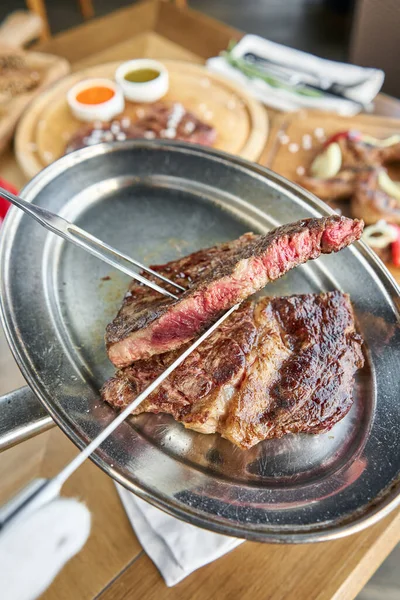 The waiter is holding a plate Grilled striploin steak with Pickled cabbage and two sauces. The strip steak, also called a New York strip. Serving on a wooden Board. Barbecue restaurant menu. — Stock Photo, Image