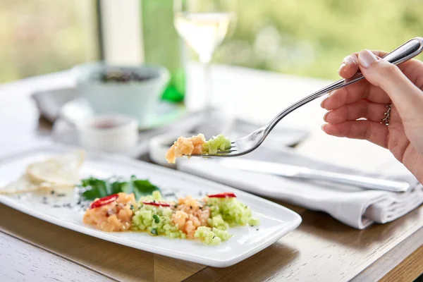 Gros plan de saumon salé et fumé ou filet de truite sur une fourchette. Tartare de saumon au concombre et graines de sésame. Plat de dégustation sur une table en bois . — Photo