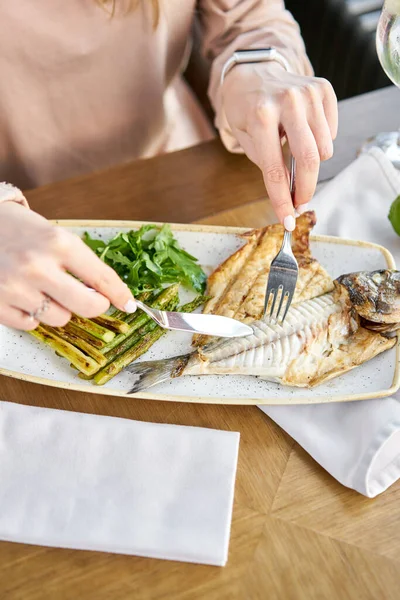 Lunch in a restaurant, a woman eats roasted dorado fish with grilled asparagus. Dish decorated with a slice of lemon. Restaurant menu — Stock Photo, Image
