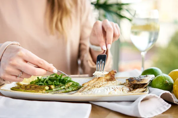 Lunch in a restaurant, a woman eats roasted dorado fish with grilled asparagus. Dish decorated with a slice of lemon. Restaurant menu — Stock Photo, Image