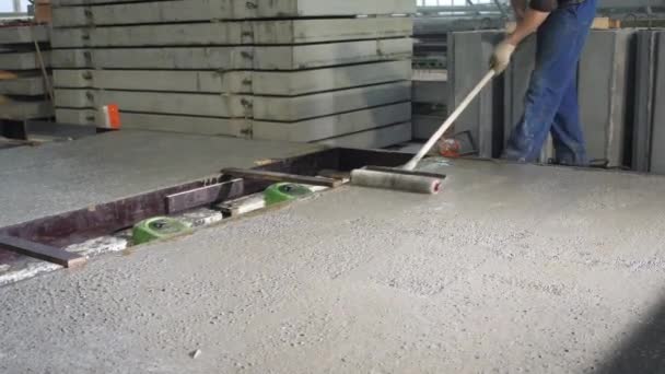 Werknemer met roller gladstrijkt cement. Werknemers in de werkplaats van de woningbouwfabriek. Industrieel interieur. Betoninstallatie. — Stockvideo