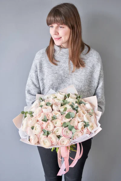 Persian buttercup in womans hands. Bunch pale pink ranunculus flowers with green eucalyptus. The work of the florist at a flower shop