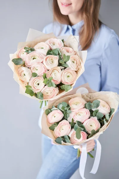 Butaca persa en manos de mujeres. Ramo de flores de ranúnculo rosa pálido con eucalipto verde. El trabajo de la floristería en una floristería — Foto de Stock