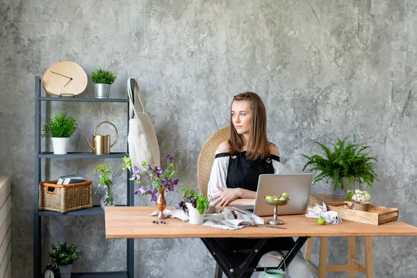 Jovem florista feminina sorridente amigável falando em um telefone celular e criar ordem na base de trabalho em um laptop. Conceito de entrega de flores. Trabalhador profissional em uma florista . — Fotografia de Stock