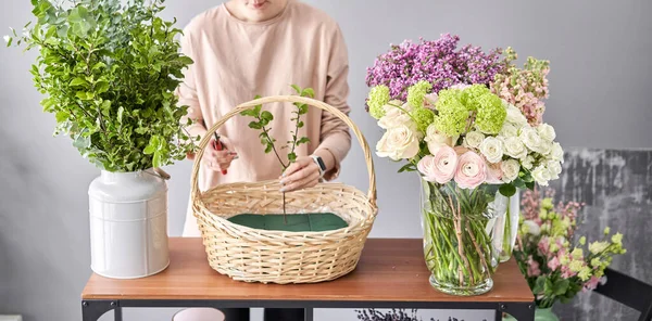 Concepto de tienda floral. Mujer florista crea arreglo floral en una canasta de mimbre. Hermoso ramo de flores mixtas. Hermoso grupo fresco. Entrega de flores . — Foto de Stock