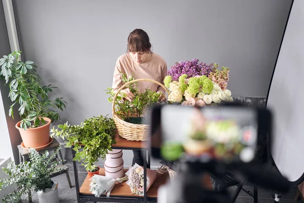 En kvinna skriver en video blogg eller online kurs. Grundskolekoncept. Blommor kvinna skapar blomsterarrangemang i en korg. Blommor leverans. — Stockfoto