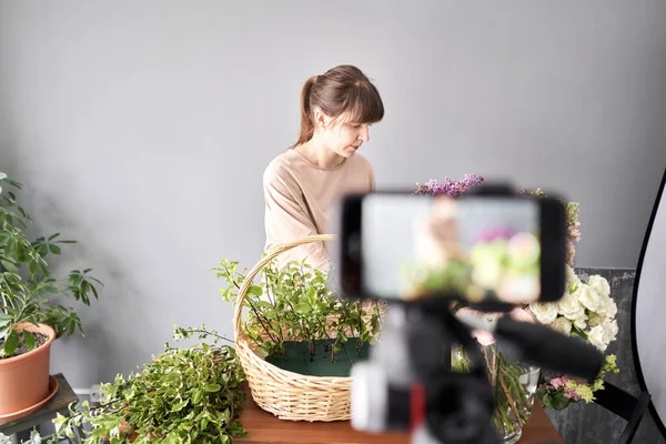 En kvinna skriver en video blogg eller online kurs. Grundskolekoncept. Blommor kvinna skapar blomsterarrangemang i en korg. Blommor leverans. — Stockfoto