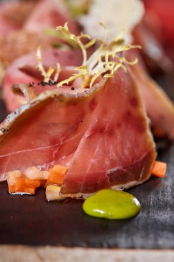 Tahta tabakta Antipasto yakın çekim. Domates soslu soğuk füme et tabağı, dilimlenmiş jambon, jambon, pastırma. Ahşap tepside aperatif. Kesilmiş ağaç taklidi..