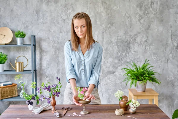 Kvinnan tittar på kameran. Ung kvinna florist skapa blomsterarrangemang Ikebana i kenzan. Använder sax och beskärare. Säsong sommar trädgård blommor. — Stockfoto