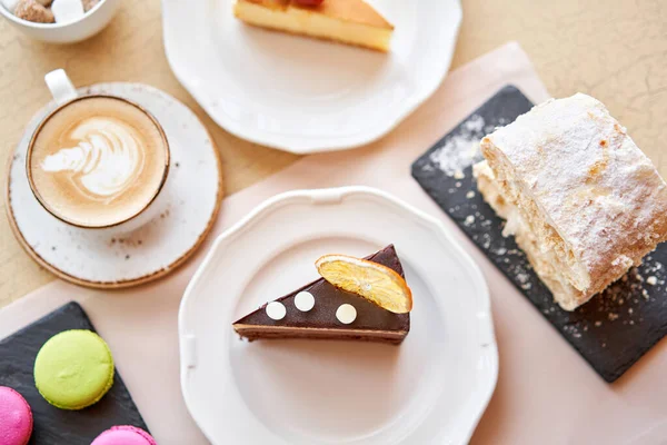 Breakfast in the cafe, morning coffee. Cappuccino and lots of desserts on the table. Napoleon, chocolate cake, cheesecake and macaroons.