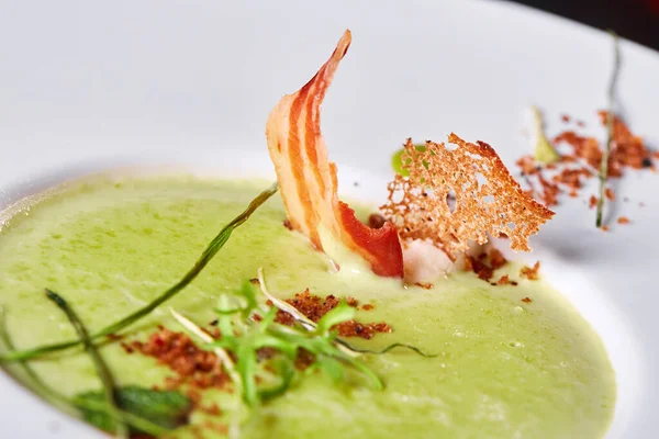 Crema vegetale minestra di piselli verdi in un piatto bianco. Minestra di purea con cracker e pancetta affumicata . — Foto Stock